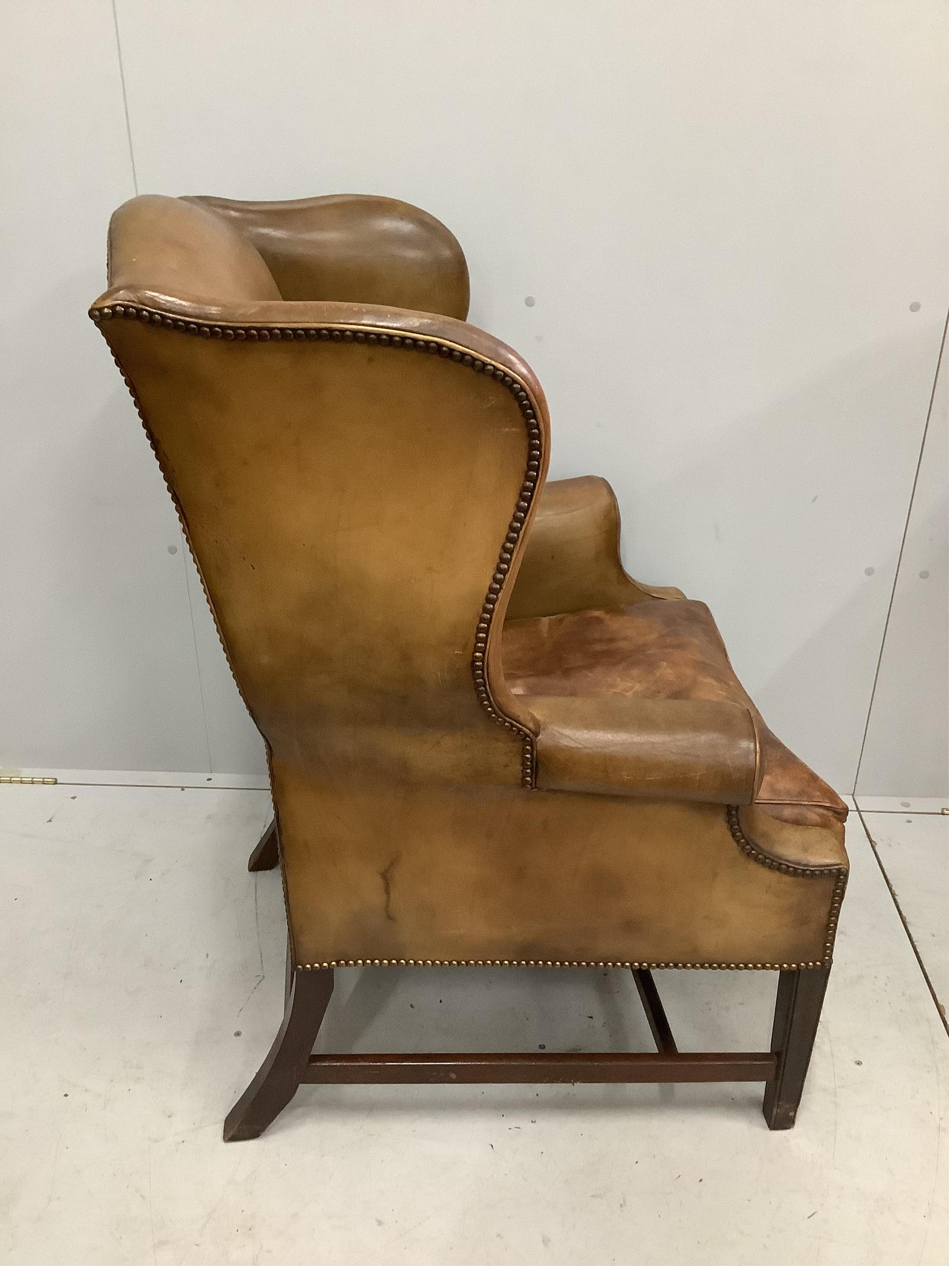 A George III style tan leather wing armchair, width 80cm, depth 68cm, height 107cm. Condition - fair